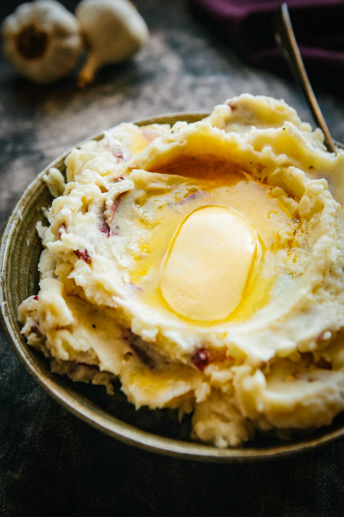 Bowl of creamy red skin mashed potatoes with melted butter on top and bits of red potato skin visible.