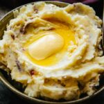 Close-up of mashed potatoes with red skins and melted butter pooling in the center.