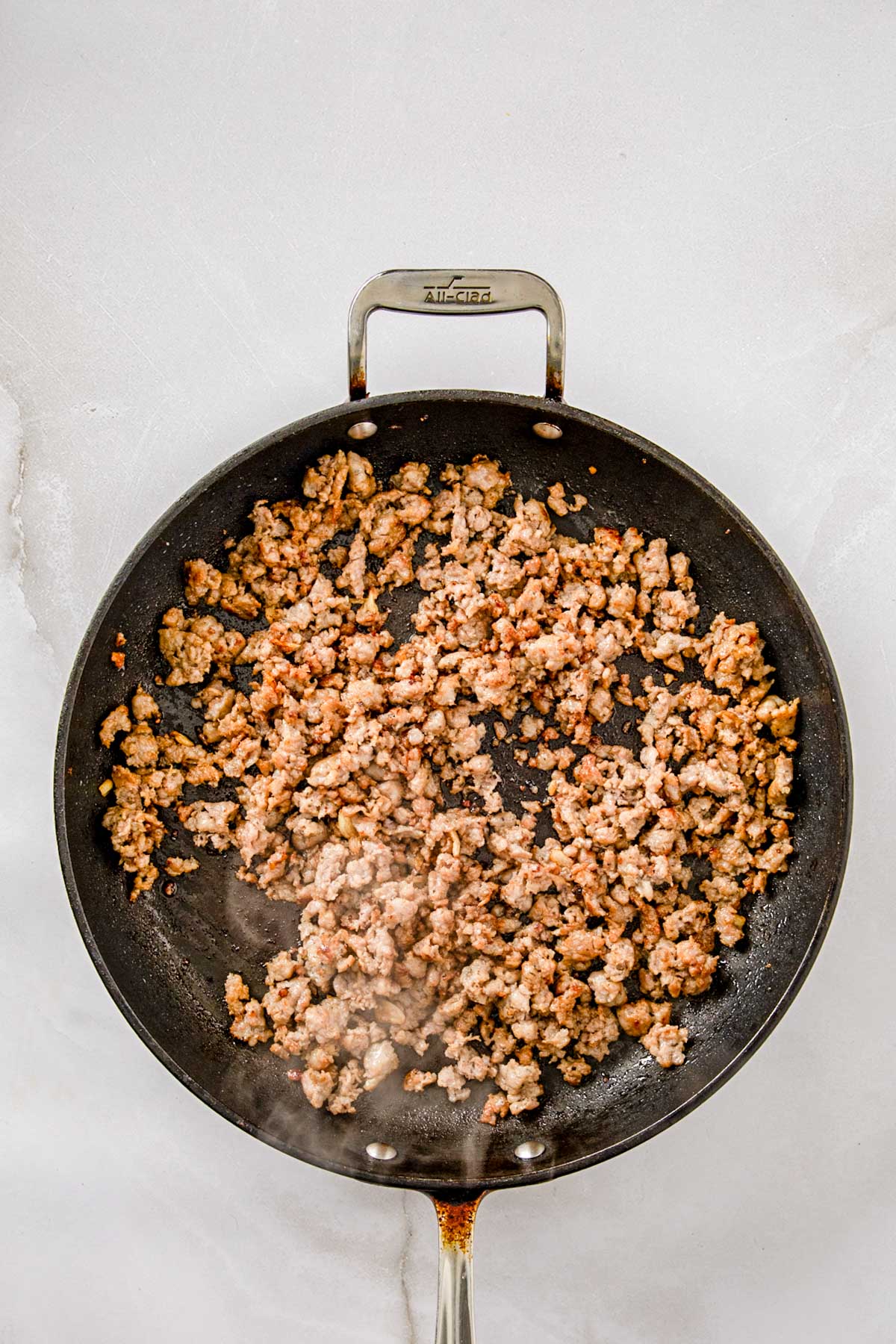 Browned Italian sausage cooking in a large skillet until crisp and golden for orecchiette with broccoli rabe.