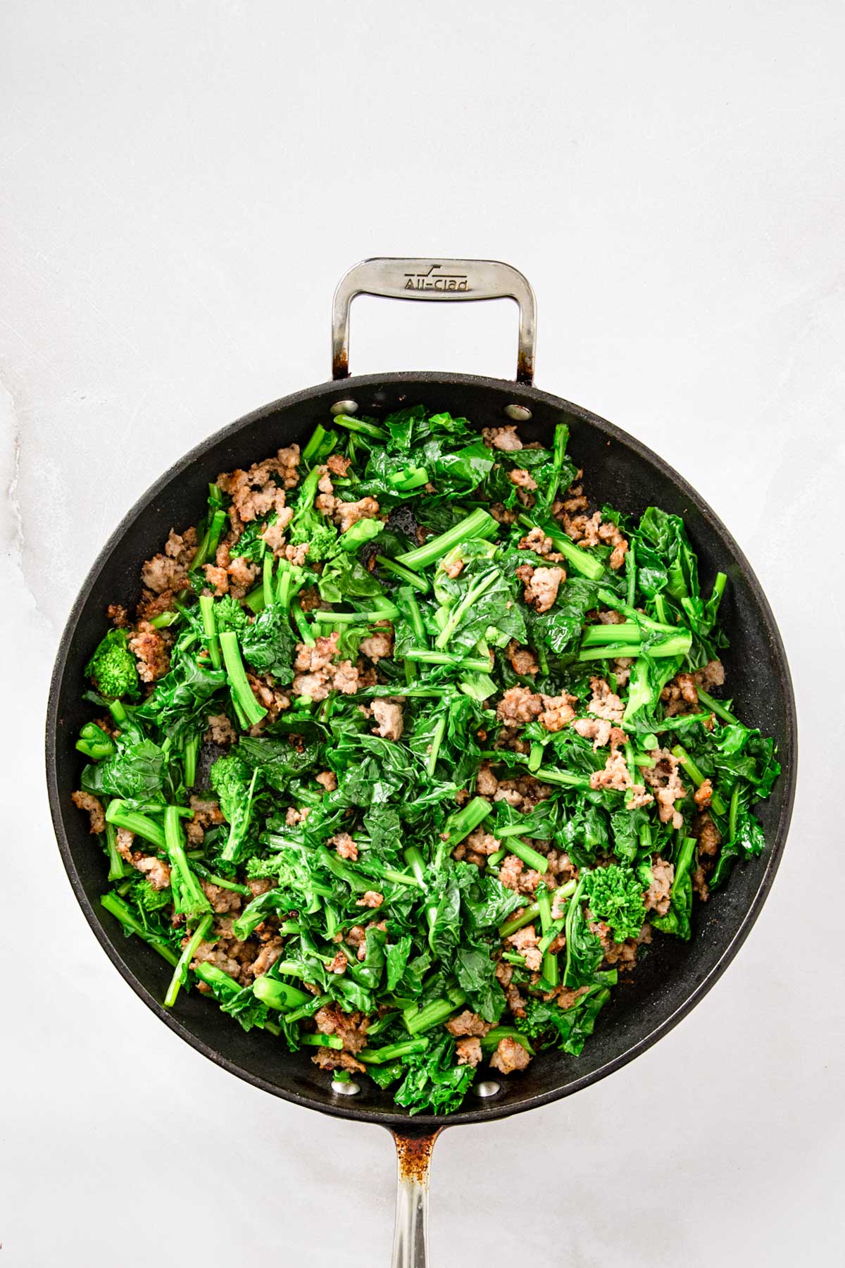 Cooked sausage and blanched broccoli rabe mixed together in a skillet over medium heat.