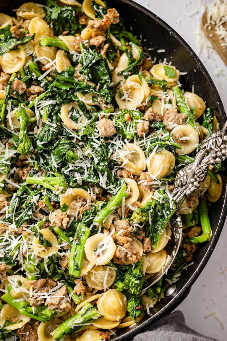 Close-up of orecchiette pasta with broccoli rabe and sausage topped with freshly grated cheese.