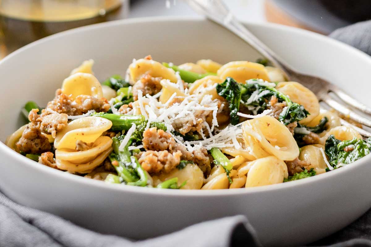 Creamy orecchiette pasta with sausage and broccoli rabe served in a white bowl with cheese on top.