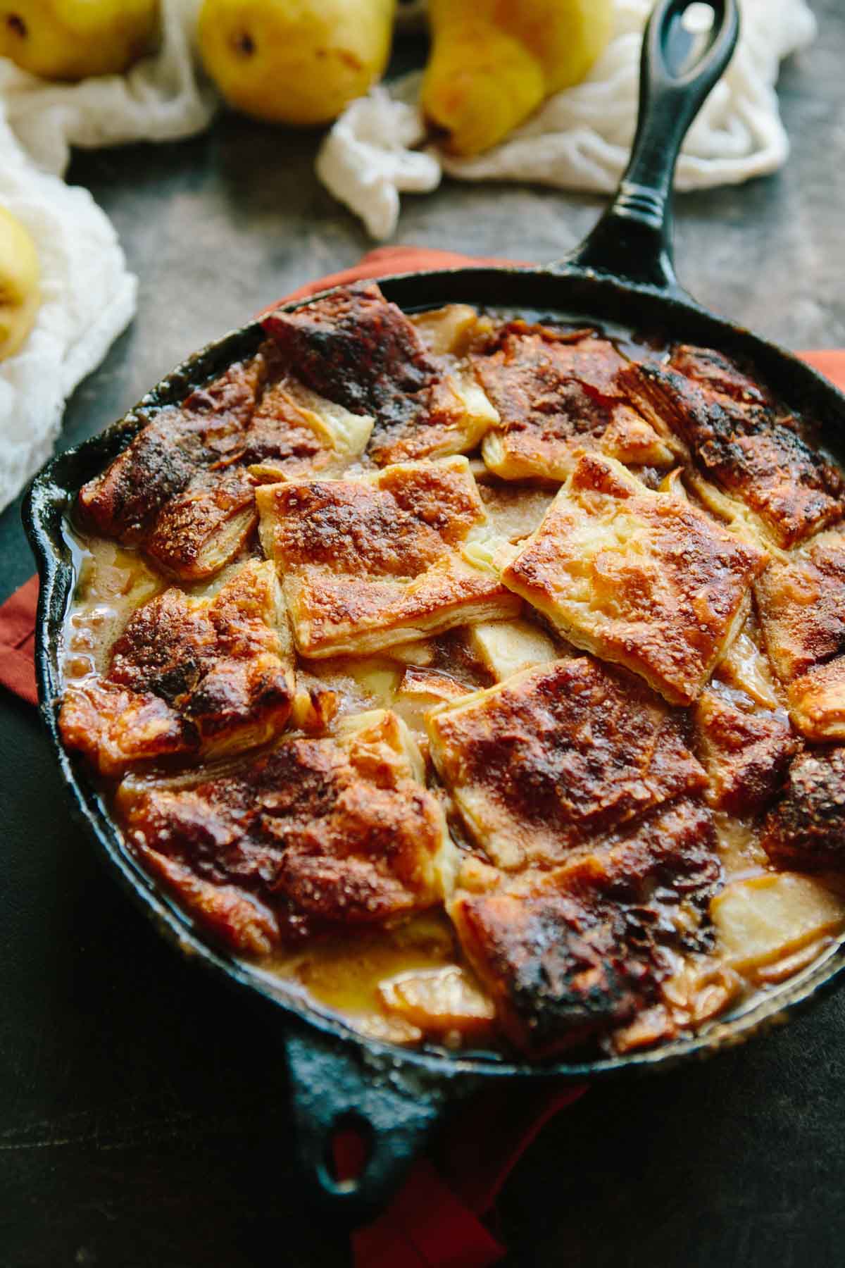 Brown butter pear pandowdy baked in a cast iron skillet with golden, caramelized puff pastry squares and bubbling pear filling.
