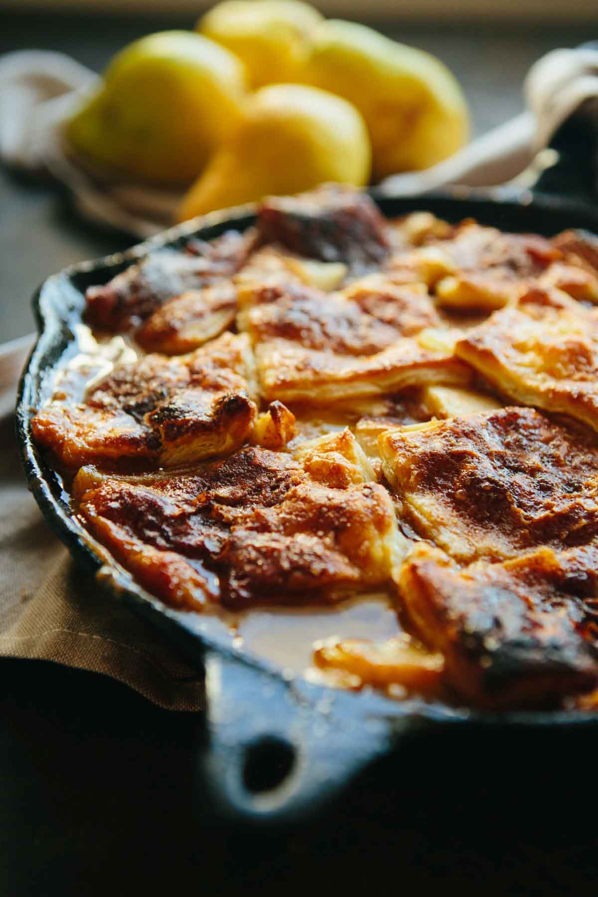 Close-up of pear pandowdy showing crisp, browned puff pastry crust with soft caramelized fruit underneath.