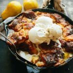Brown butter pear pandowdy topped with melting scoops of vanilla ice cream in a cast iron skillet.