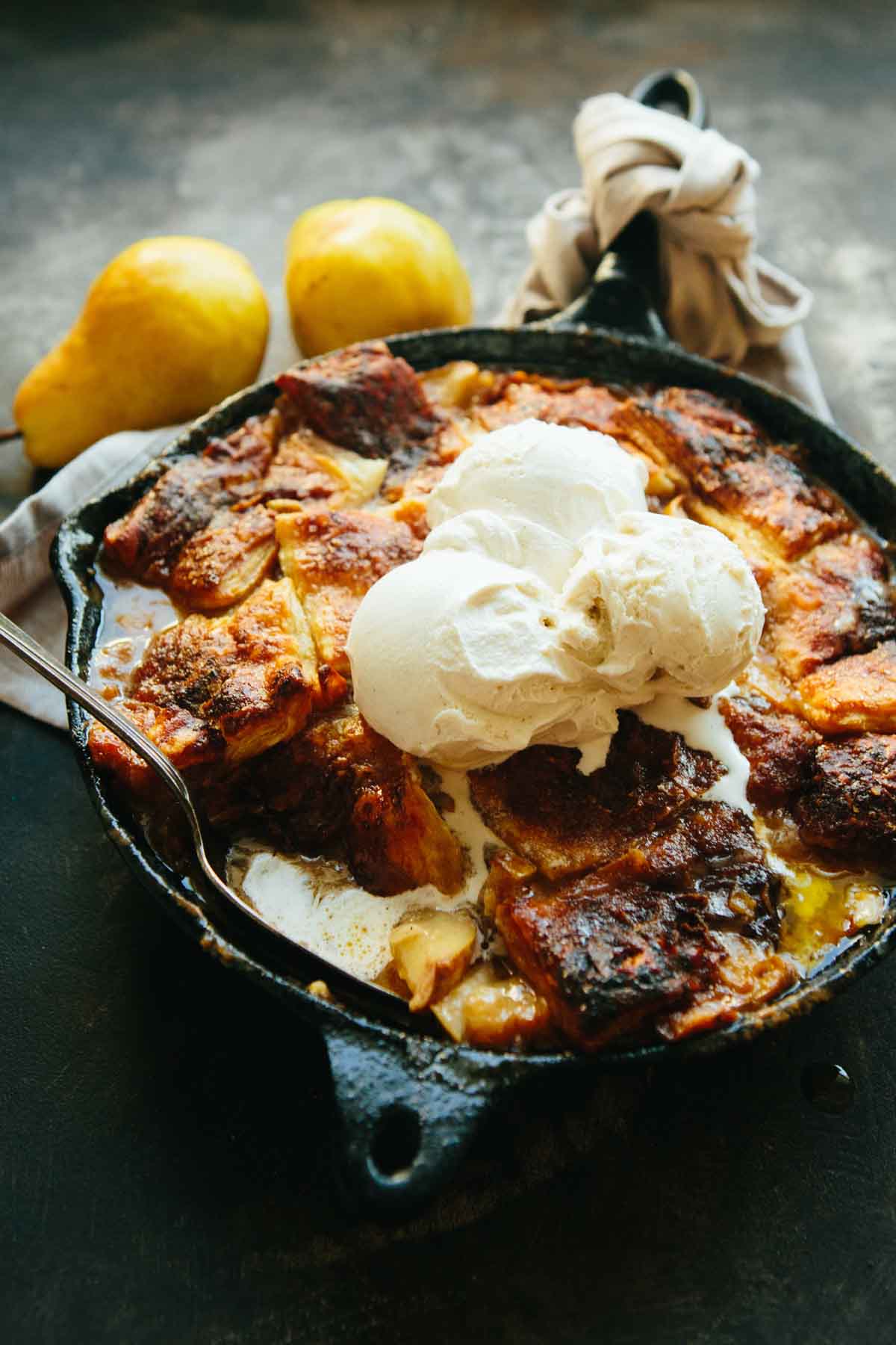 Brown butter pear pandowdy topped with melting scoops of vanilla ice cream in a cast iron skillet.