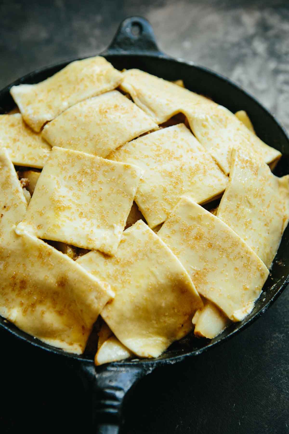 Unbaked pear pandowdy with puff pastry dough squares brushed with egg wash and sprinkled with coarse sugar.