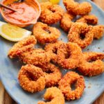 Angled shot of golden brown fried shrimp on a platter showing texture of the crust.