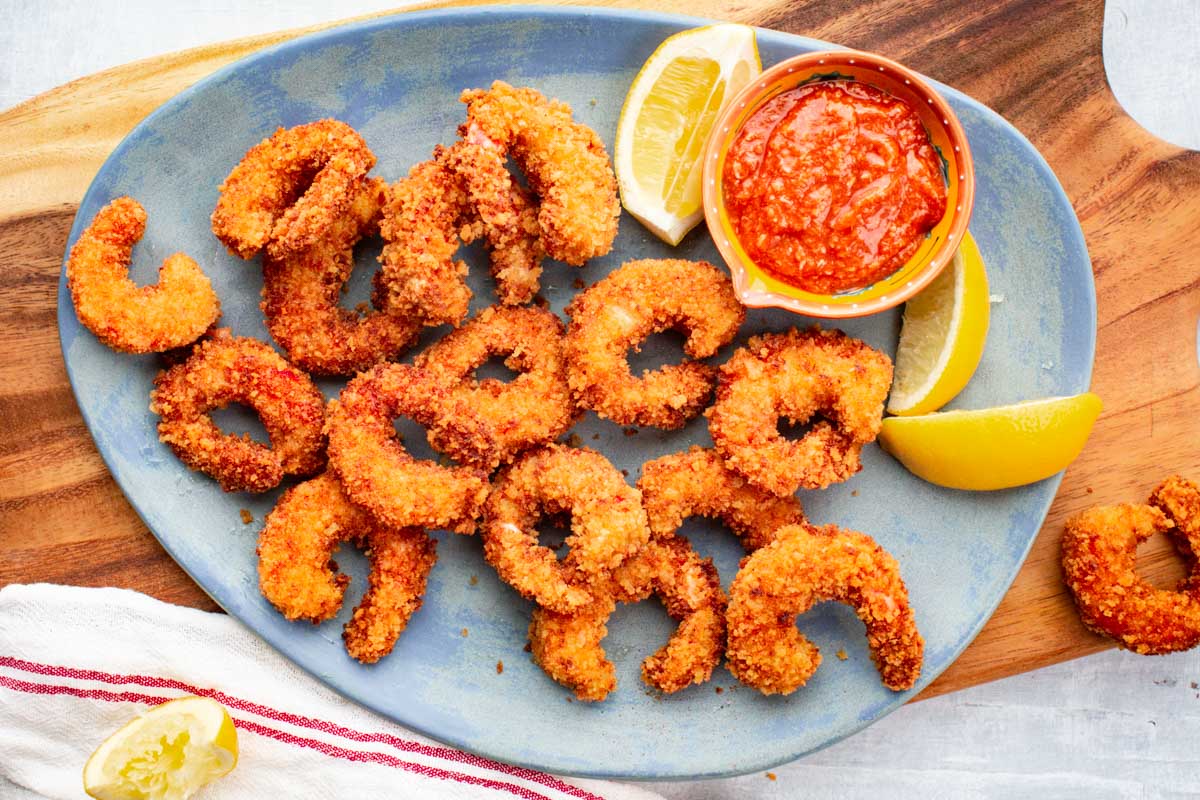 Hand holding a spider skimmer lifting a piece of fried shrimp over a pot of hot oil.
