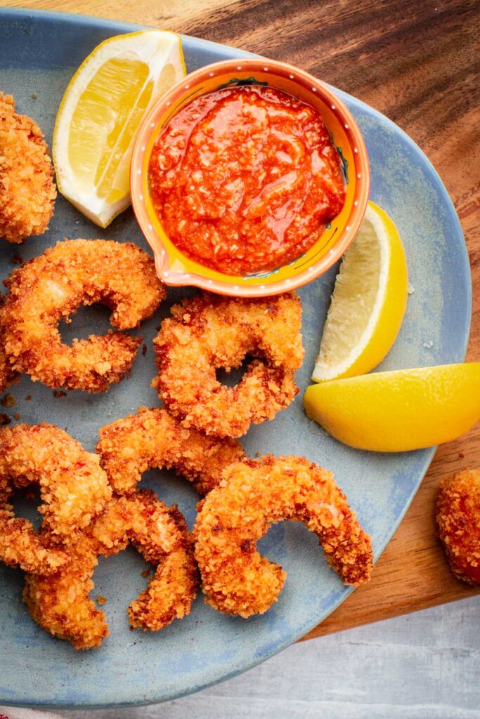Finished fried shrimp arranged on a blue platter with lemon wedges and cocktail sauce.