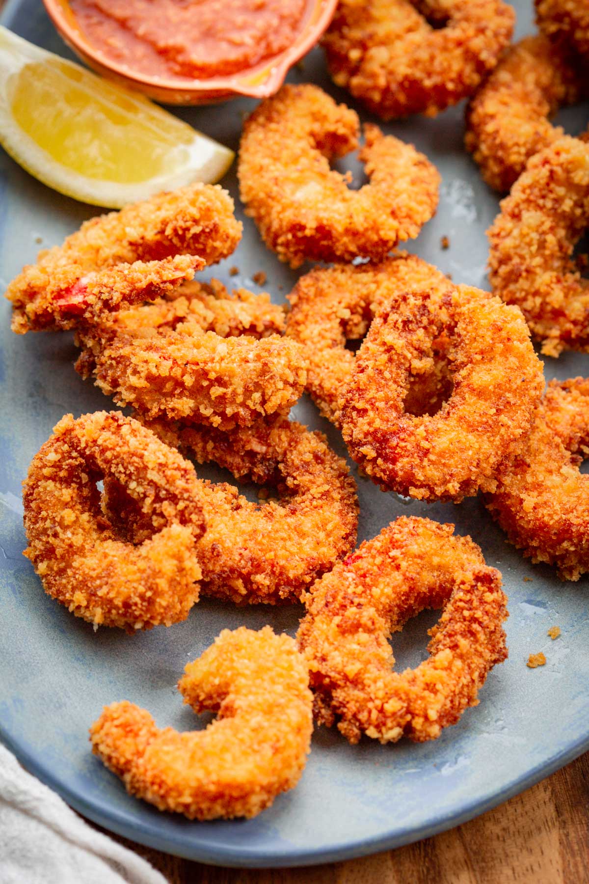 Close-up of crispy panko crusted shrimp with cocktail sauce and lemon slices.