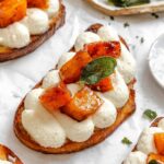 Finished pumpkin ricotta crostini topped with caramelized squash and fried sage leaves arranged on parchment paper.