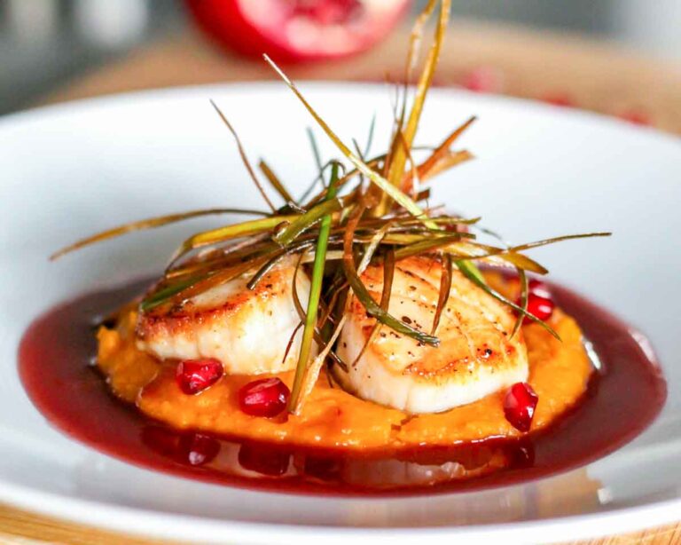 Seared scallops with pomegranate beurre blanc sauce, served over squash purée and topped with crispy leeks.