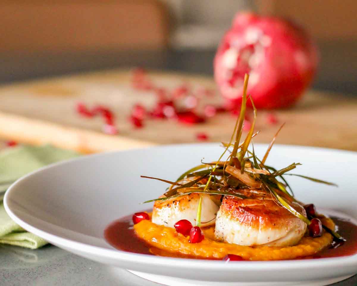 Side view of scallops with pomegranate beurre blanc and fresh pomegranate seeds.