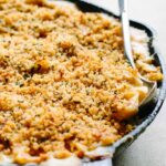 Cast iron skillet filled with mac and cheese topped with toasted panko crumbs and a serving spoon.