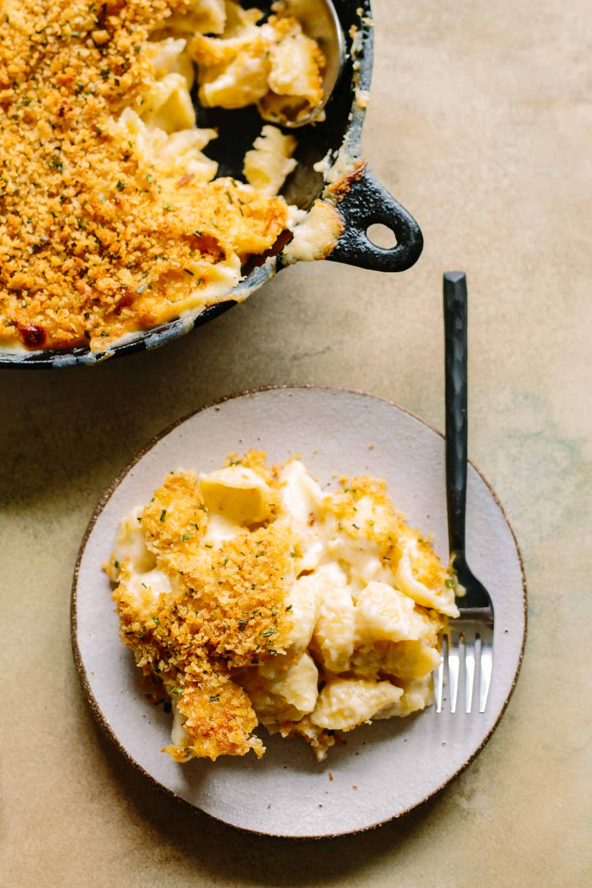 Overhead view of skillet mac and cheese and a serving on a plate with a fork.