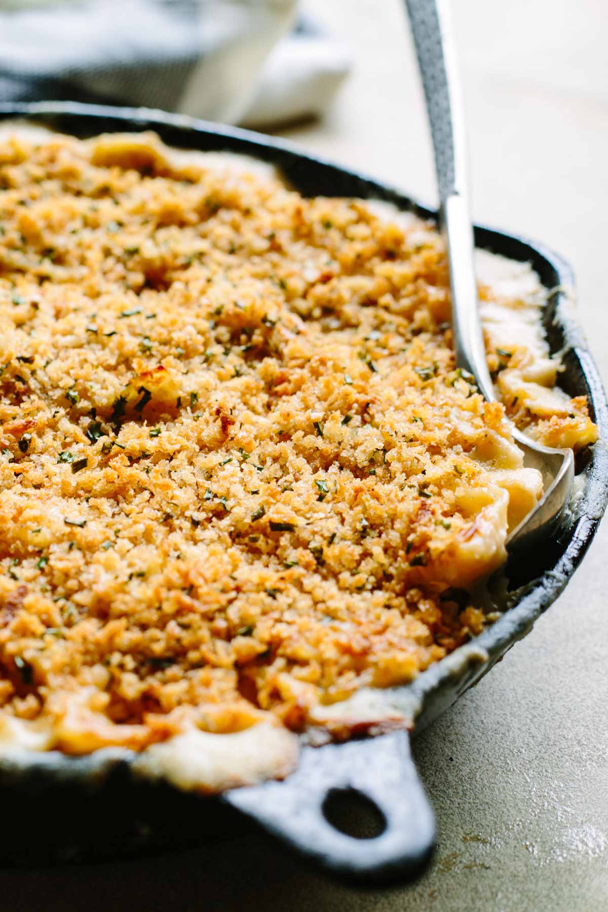 Cast iron skillet filled with mac and cheese topped with toasted panko crumbs and a serving spoon.