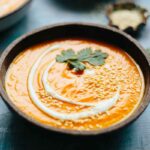 Bowl of spicy carrot soup garnished with sesame seeds and cilantro, photographed at an angle with habanero peppers in the background.