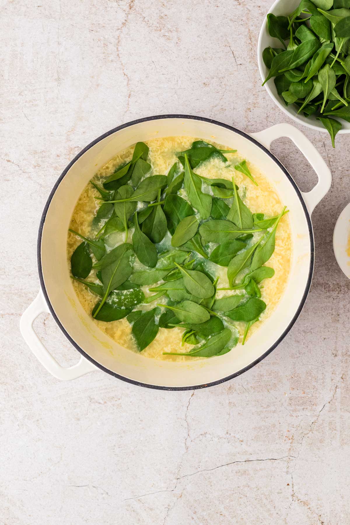 Baby spinach leaves added into the pot of broth and eggs, floating on top of the simmering soup.