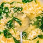 Zoomed-in view of stracciatella soup showing fluffy shreds of egg and tender spinach leaves in a clear broth.