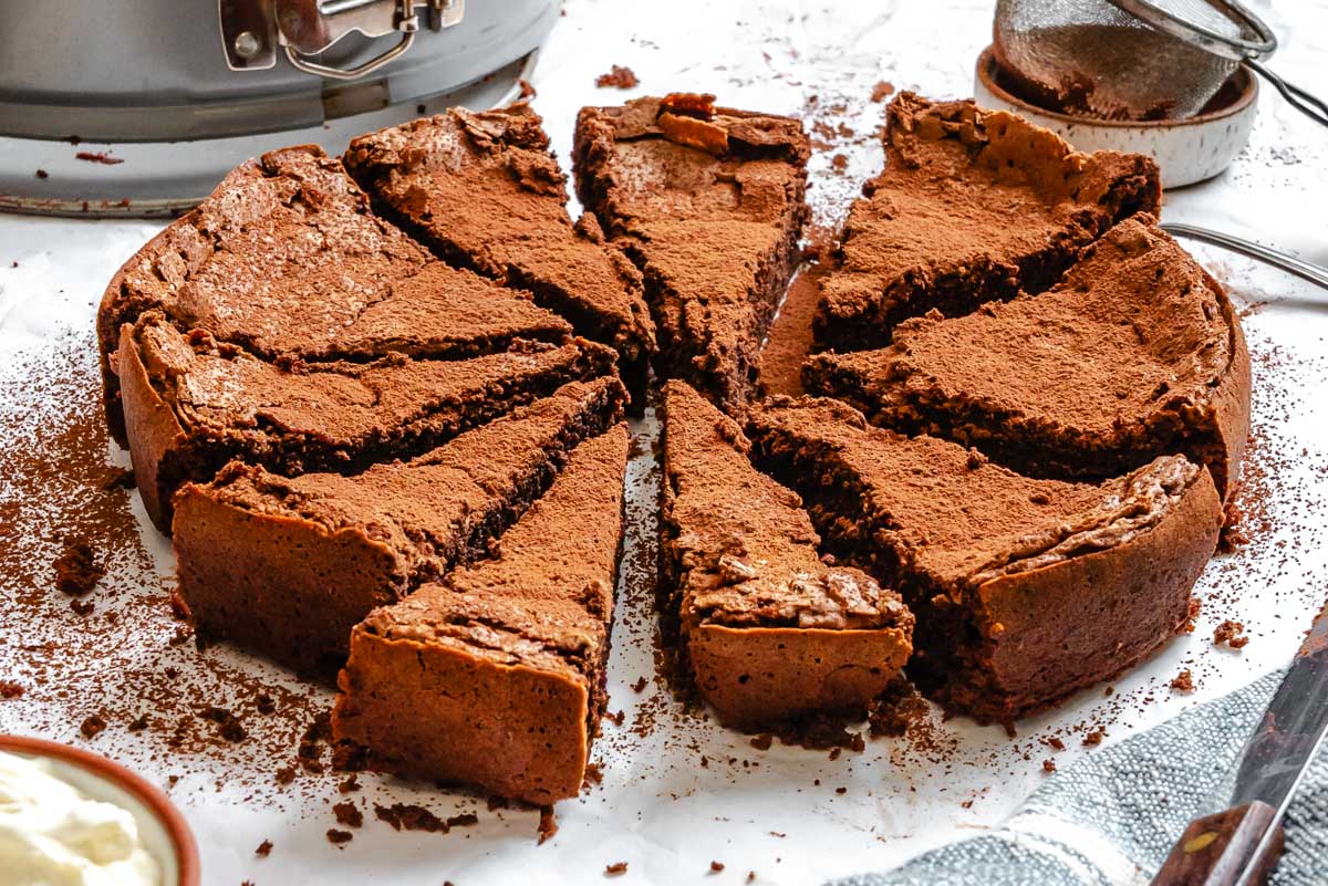 Close-up side view of a rich, fudgy Torta Caprese cut into wedges, showing its crackly top and dense interior coated in cocoa powder.