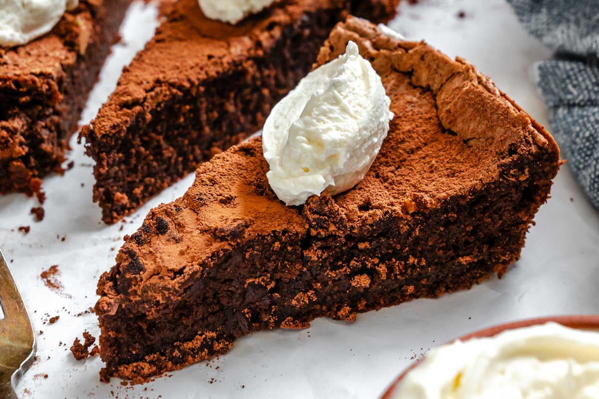 Detailed slice of Torta Caprese topped with a dollop of whipped cream, highlighting its moist crumb and deep chocolate color.