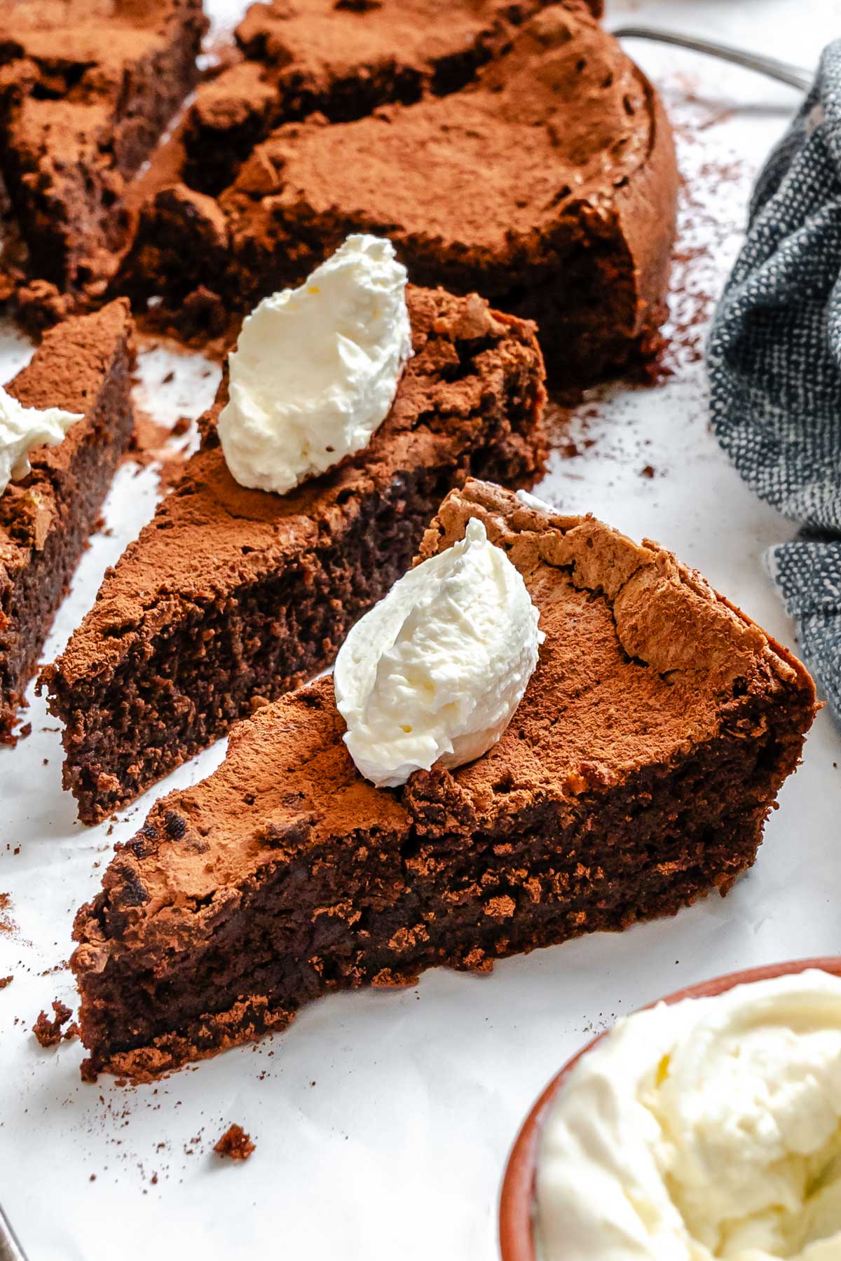 Multiple slices of Torta Caprese served with whipped cream, showcasing the cake's soft, fudgy texture and crisp cocoa-dusted top.