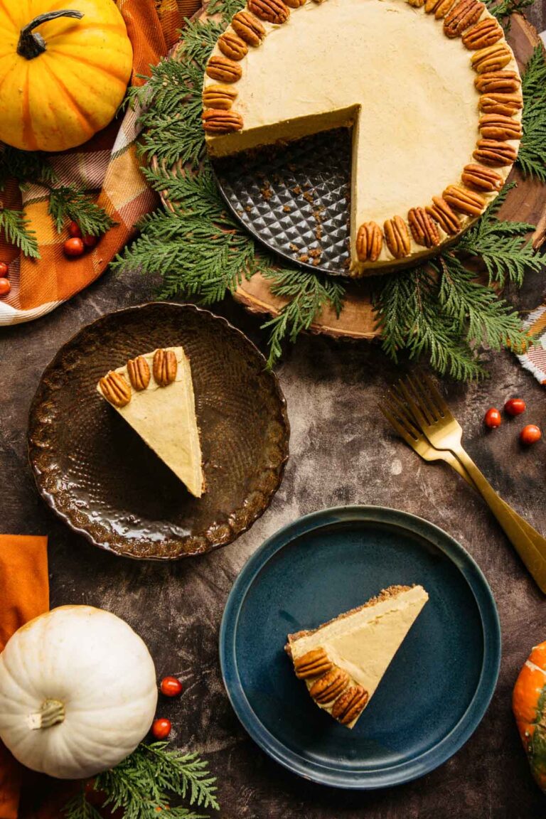 Overhead view of a vegan pumpkin cheesecake garnished with pecans, surrounded by pumpkins and greenery on a rustic table.