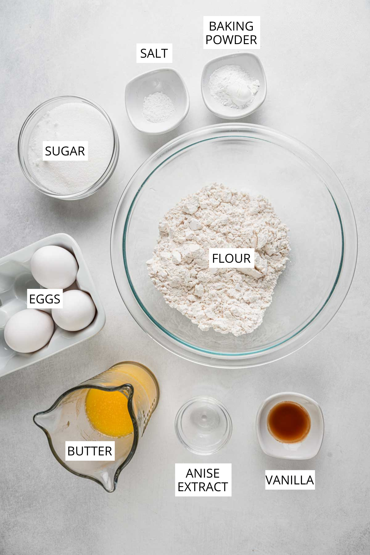Flour, eggs, sugar, melted butter, baking powder, salt, vanilla and anise extract arranged in bowls and labeled overhead for pizzelle prep.
