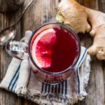 Overhead view of a Blueberry Ginger Hot Toddy with a lemon slice floating on top, surrounded by fresh ginger, blueberries, and honey on a wooden table.