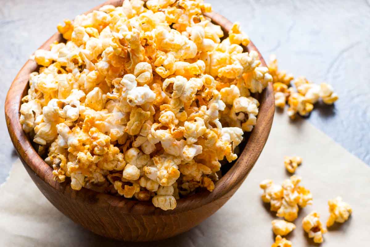 Wooden bowl filled with honey butter buffalo popcorn with pieces scattered on parchment.