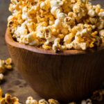 Large wooden bowl filled with honey butter buffalo popcorn showing golden coating.