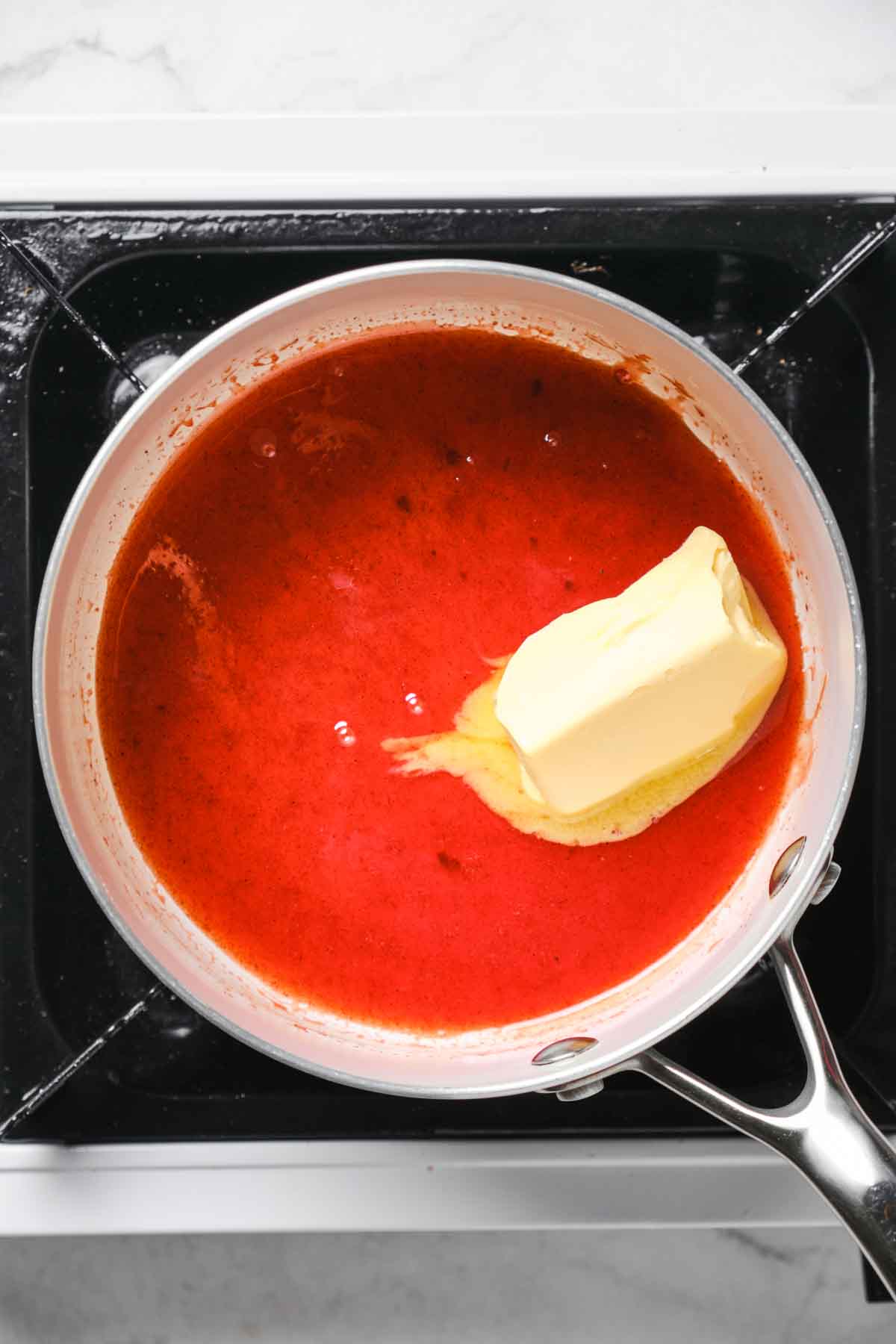 Small saucepan on stovetop with melted butter blending into bright red hot sauce to make buffalo sauce.