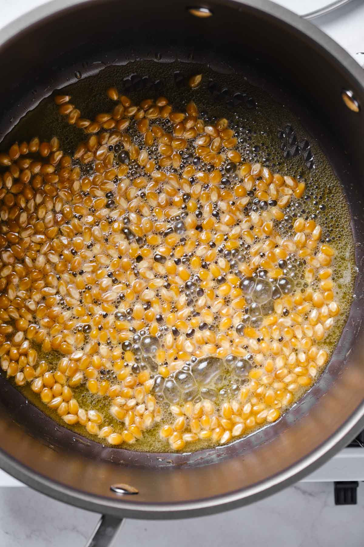 Popcorn kernels sizzling in melted butter and oil before they start to pop.