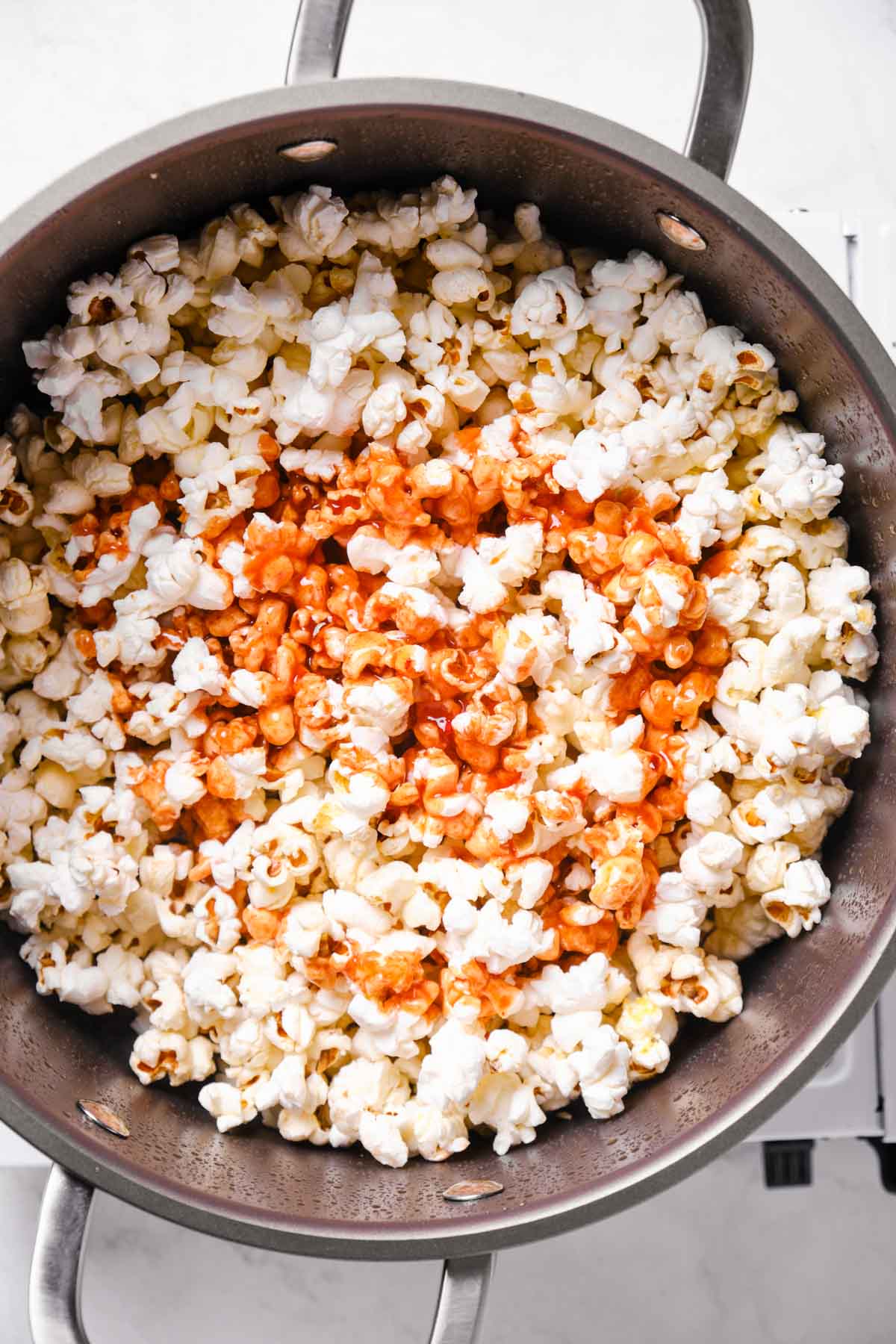 Warm popcorn in a pot being coated with honey butter buffalo sauce.