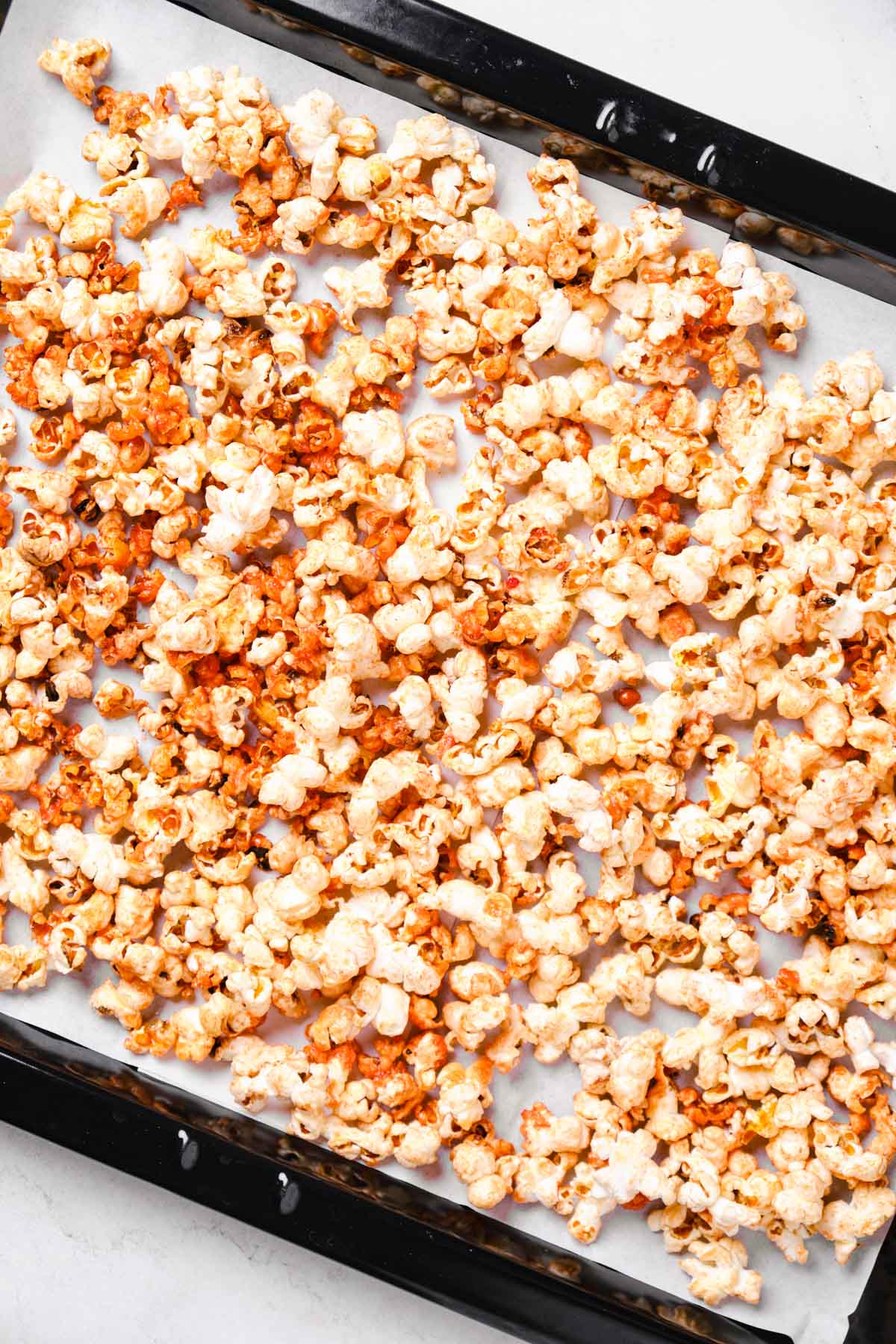Popcorn spread out on a parchment-lined baking sheet ready for the oven.