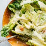 Close view of romaine leaves coated in dressing with grated parmesan and a few visible croutons in a wooden bowl.