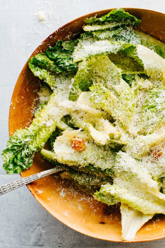 Close view of romaine leaves coated in dressing with grated parmesan and a few visible croutons in a wooden bowl.