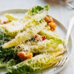 Tight close up of romaine leaves, golden croutons and grated parmesan piled on a white plate.