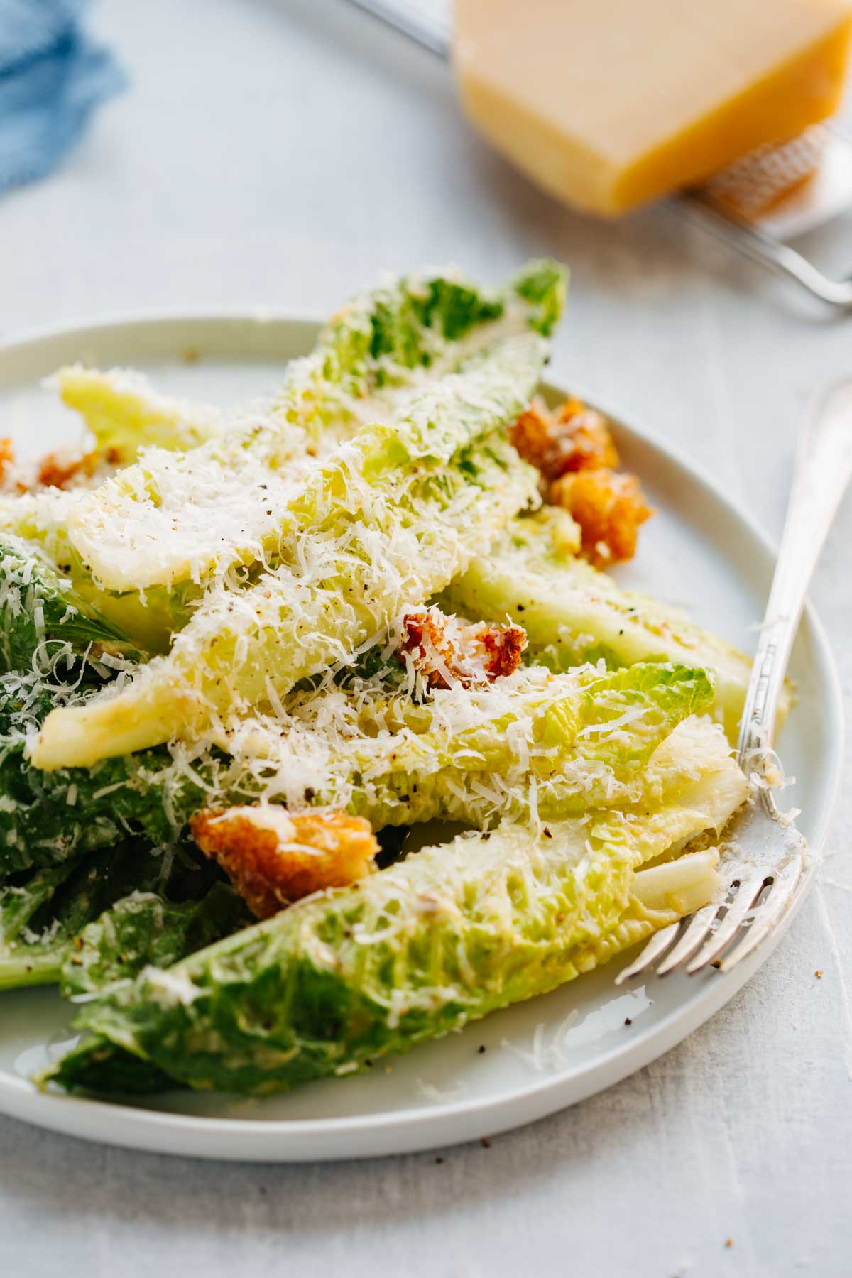 Tight close up of romaine leaves, golden croutons and grated parmesan piled on a white plate.
