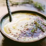 A side view of the smooth parsnip cauliflower soup with olive oil swirled on top, puffed quinoa scattered across the surface and a spoon resting in the bowl.