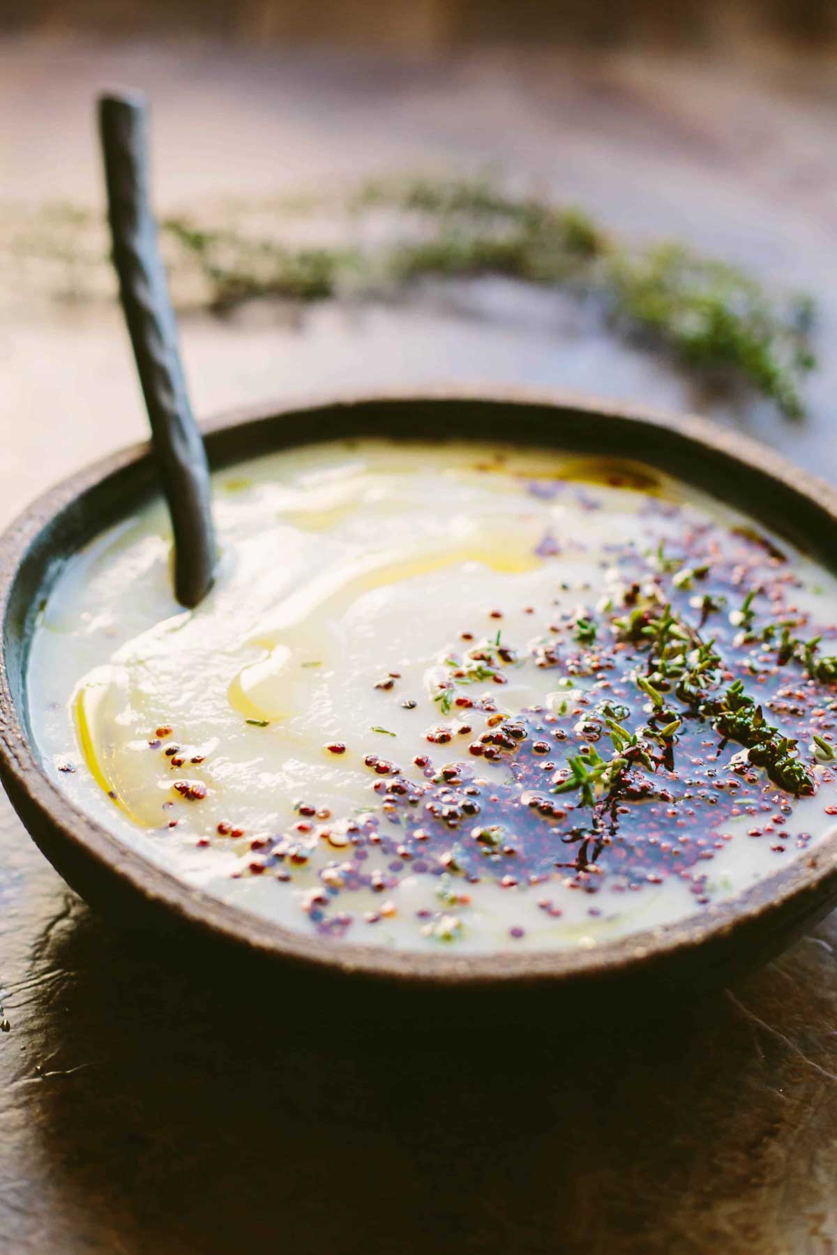 A side view of the smooth parsnip cauliflower soup with olive oil swirled on top, puffed quinoa scattered across the surface and a spoon resting in the bowl.