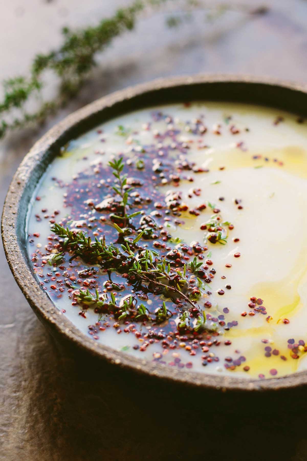 A close up of the soup showing the silky texture, glossy olive oil, scattered quinoa and fresh thyme leaves along the edge of the bowl.