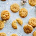 Chai snickerdoodles on a light surface with holiday decorations and one cookie broken open to show the soft center.
