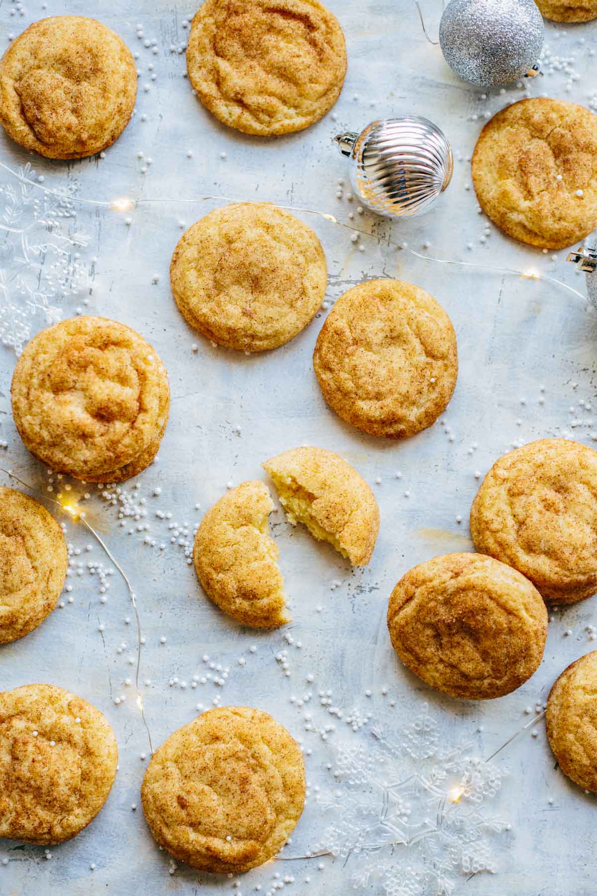 Chai snickerdoodles on a light surface with holiday decorations and one cookie broken open to show the soft center.