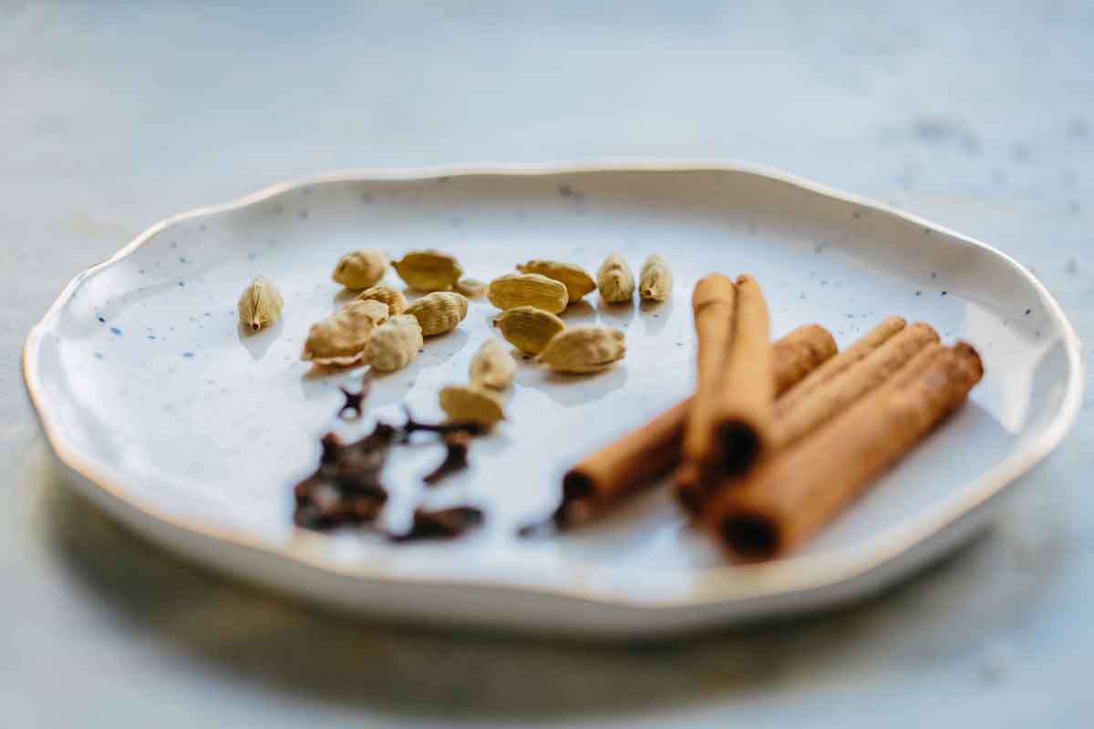 Plate with whole cardamom pods, cinnamon sticks, and cloves used for the chai spice blend.