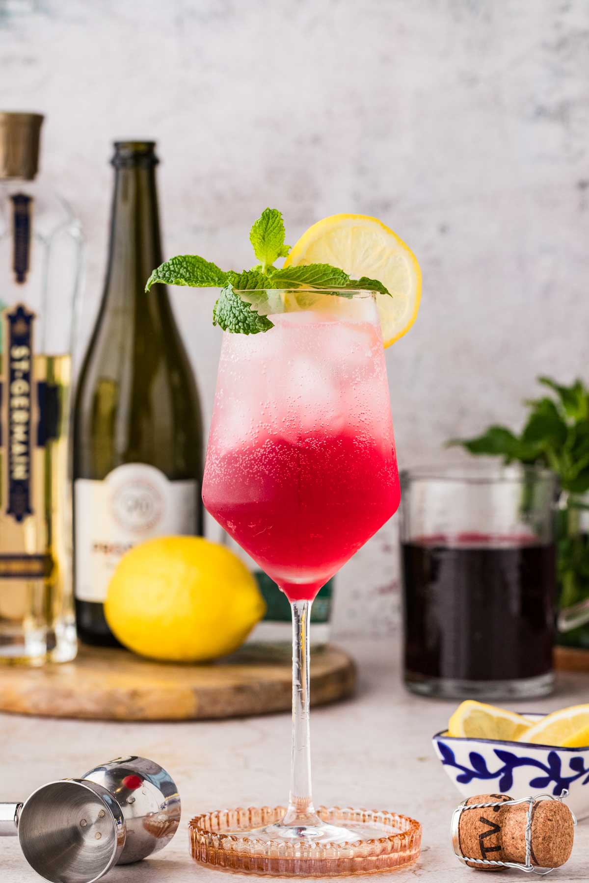 Finished Cranberry Hugo Spritz garnished with mint and lemon, showing layered pink color and effervescent bubbles.
