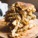 Stack of French Onion Grilled Cheese sandwiches on a wooden board, filled with gooey melted cheese and caramelized onions spilling out.
