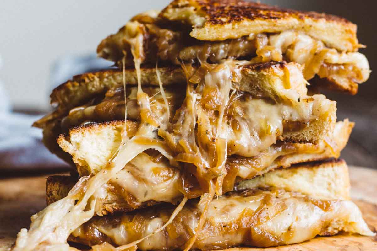 Close-up of grilled cheese sandwiches oozing melted Gruyère and sweet caramelized onions, golden and crisp on the edges.