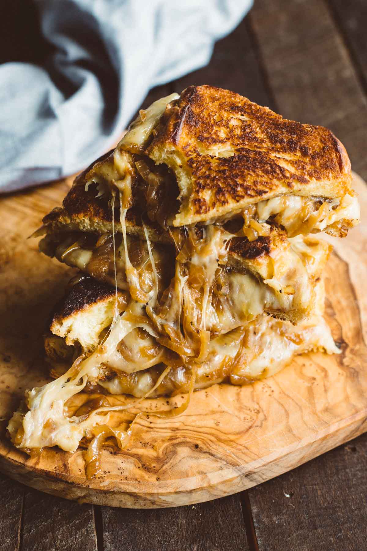 Overhead view of stacked French Onion Grilled Cheese sandwiches with jammy onions and melted cheese on a rustic wood surface.